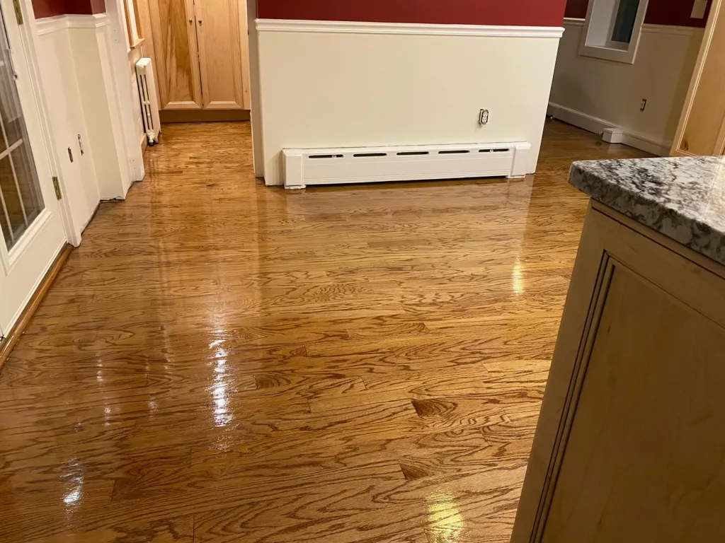 View of a kitchen and dining area displaying the results of hardwood floor refinishing, with a glossy finish reflecting light.