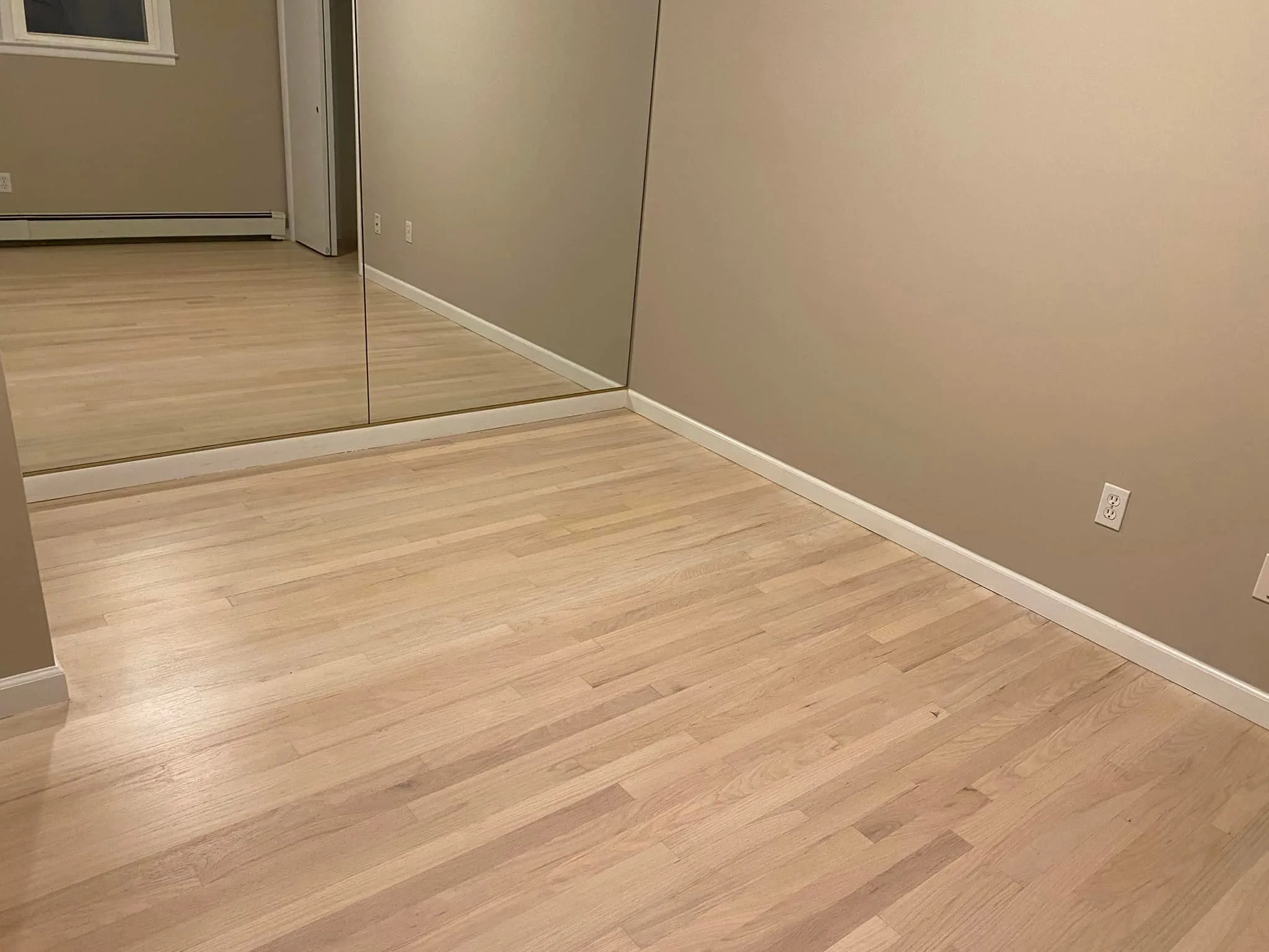 Another view of the clean, natural-toned wood floor post-hardwood floor sanding, looking toward a large mirrored wall and a closet door.