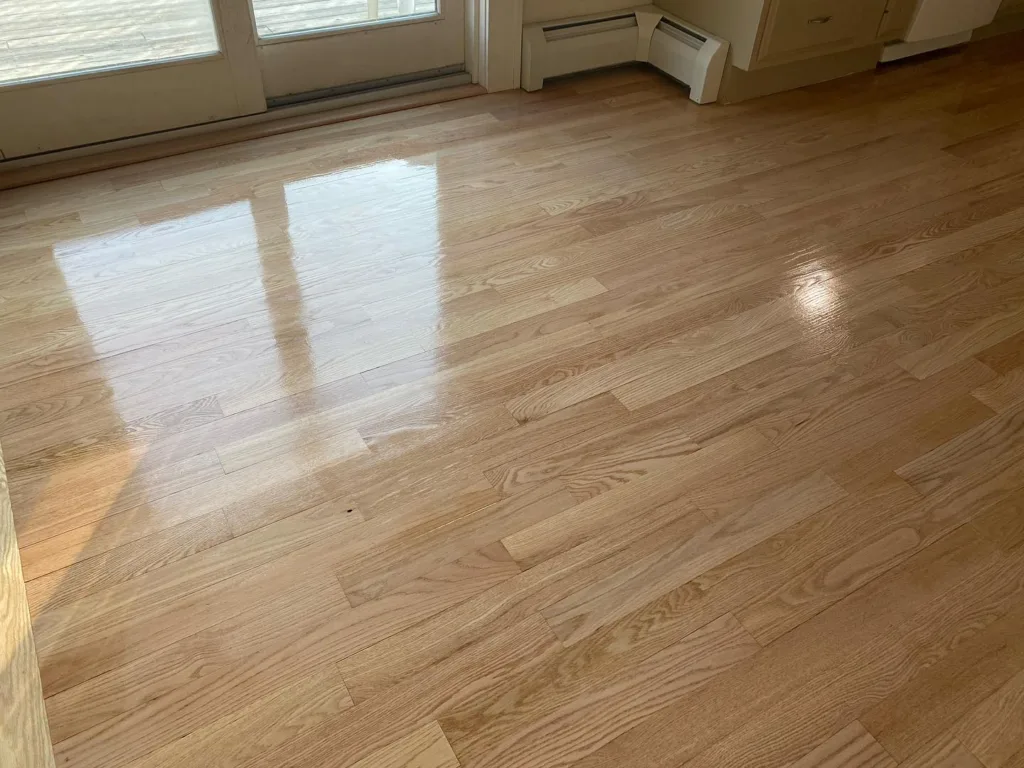 Natural light illuminating the smooth, reflective surface of newly completed oak floor refinishing near a patio door.